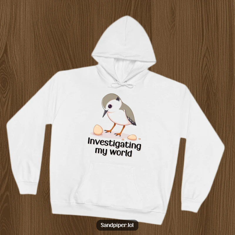 Funny hoodie featuring a sandpiper character inquisitively pecking at a small shell, symbolizing a love for discovery.