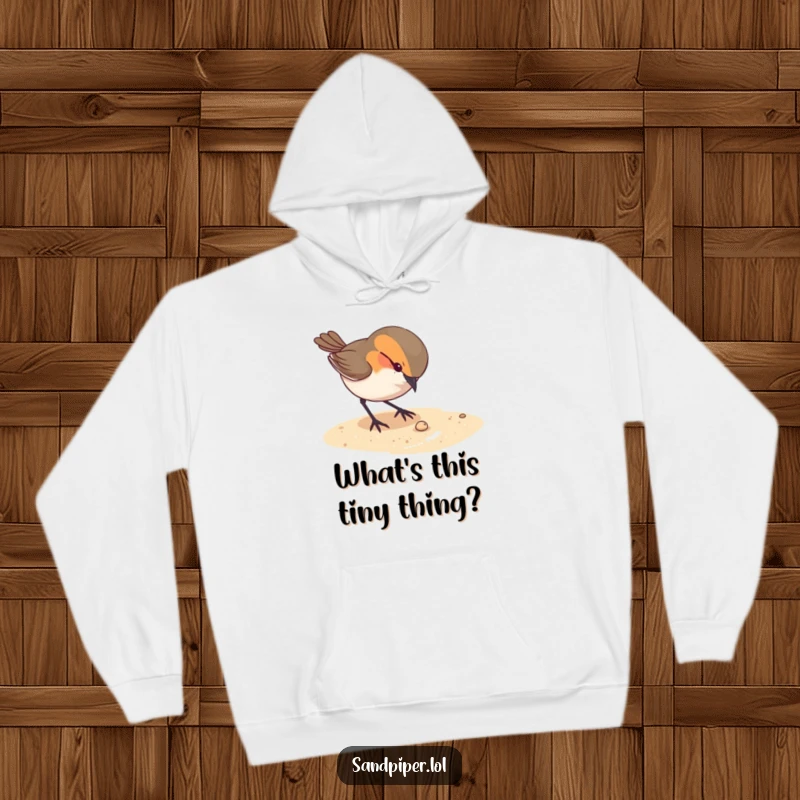 Funny hoodie depicting a curious bird pecking at something tiny on the sandy ground, offering cozy contemplation.